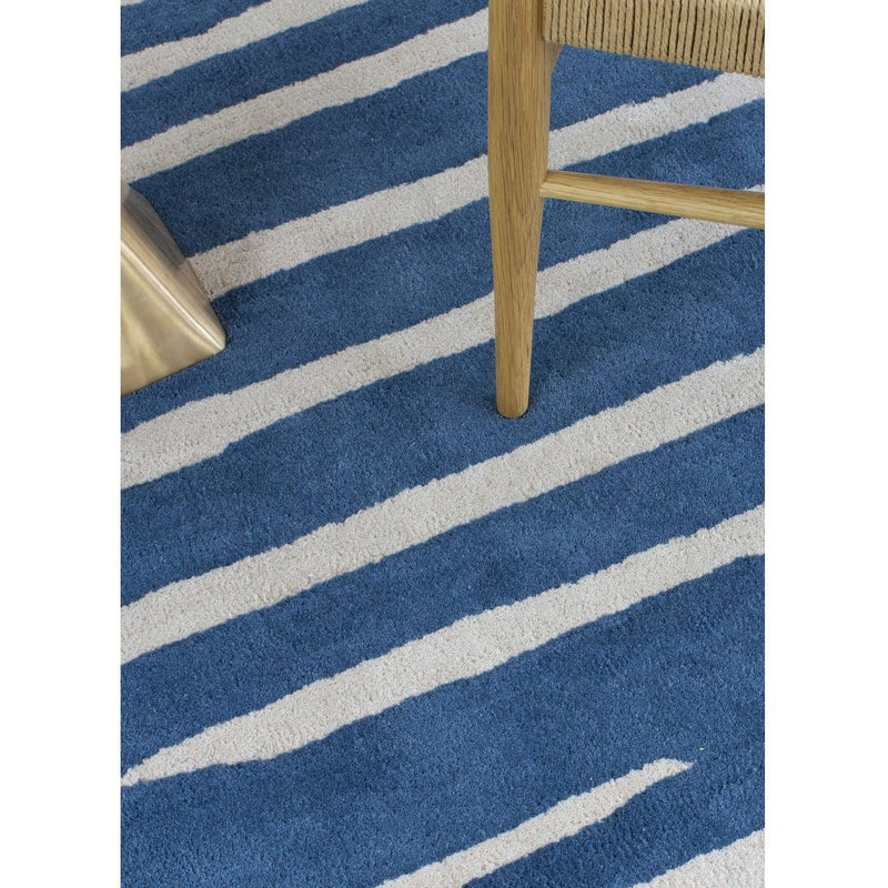 Island Blue Rug is an abstract lines patterned rug in two colours, blue and cream. The abstract lines pattern creates a circle shaped design within this rectangular wool rug. Rug close up.