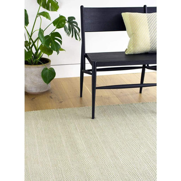 Tibba Fern Rug is a green recycled plastic bottle rug handwoven from 100% repurposed. The herringbone style weave is suited to modern and traditional homes. Rug styled with chair and plant.