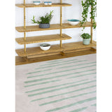 Island Leaf Rug is an abstract lines patterned rug in two colours, cream and green. The abstract lines pattern creates a circle design within this rectangular wool rug. Pictured with bookshelves. 