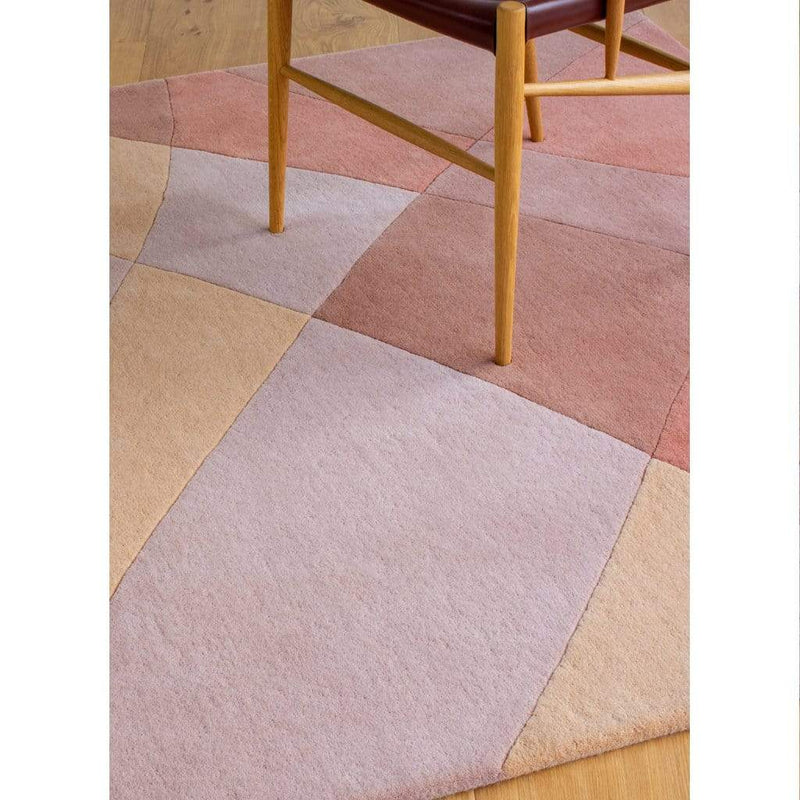 Rhythmic Tides Sand Rug is designed in warm earthy terracotta and pink colours and features a curved pattern to depict the ebb and flow of the tides. Rectangular rug shown with chair.