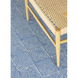 Zala Denim Rug - a blue recycled rug, handloom woven from 100% recycled plastic bottles. Our sustainable rugs are helping to combat plastic waste by using hundreds of recycled plastic bottles for each rug. Rug close up with wooden chair.