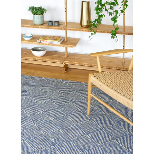 Zala Denim Rug - a blue recycled rug, handloom woven from 100% recycled plastic bottles. Our sustainable rugs are helping to combat plastic waste by using hundreds of recycled plastic bottles for each rug. Rug pictured with bookshelves and chair.