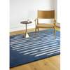 Island Blue Rug is an abstract lines patterned rug in two colours, blue and cream. The abstract lines pattern creates a circle shaped design within this rectangular wool rug. Pictured with chair and side table.